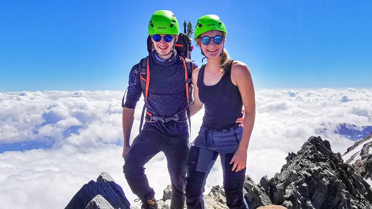 Zwanzigjähirger Frau und Mann stehen mit Wanderausrüstung auf dem Gipfel eines Berges. 