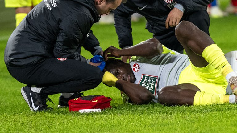 Ragnar Ache (1. FC Kaiserslautern) wird am Boden liegend behandelt, nachdem ihn eine geworfene Flasche getroffen hat