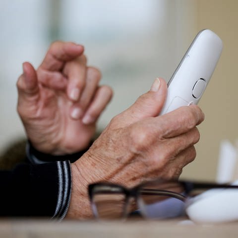 Eine Hand hält ein Telefon. Symbolbild Trickbetrüger.