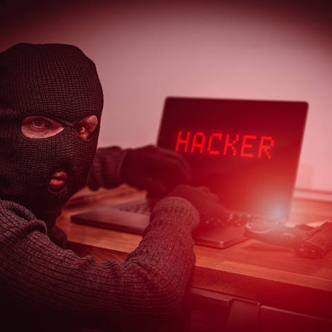 Das Bild zeigt einen Mann mit Skimaske vor einem Rechner. Auf dem Bildschirm steht "Hacker".